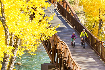 A mother and daughter mountain biking over the Animas River on a bridge on the Animas River Trail in Durango, Colorado.