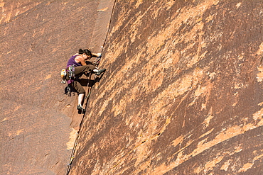 A woman rock climbing up a layback crack at a rock climbing area called The Wall in Indian Creek, Monticello, Utah.