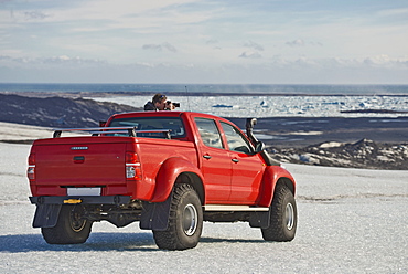 Man stopping and taking a picture from a customised Icelandic 4x4 pick up truck on the Breidamerkurjokull glacier, which is a part of the Vatnajokull glacier