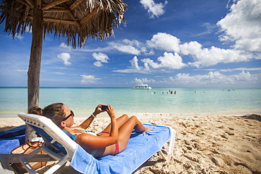 A young woman takes a picture with her smartphone while relaxing on the beach during a vacation in Cayo Coco, Cuba.