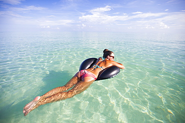 A young woman floats on an inflatable water toy in shallow turquoise water while on vacation in Cayo Coco, Cuba.