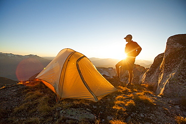 A silhouetted hiker partially blocks he sunset while camping on Saxifrage Peak, Pemberton, BC, Canada.