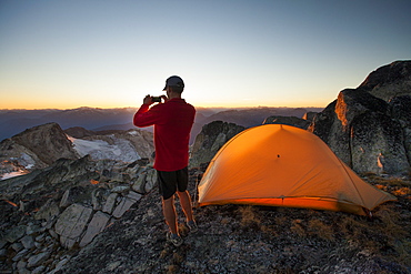 A hiker takes a picture of the sunset with his smartphone while camping on the summit of Saxifrage Peak, Pemberton, BC, Canada.