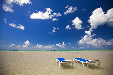 Two empty beach chairs sit in ankle deep water facing the turquoise ocean in Cayo Coco, Cuba.