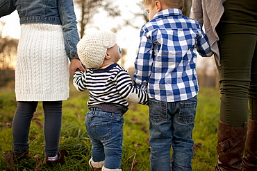 A baby girl looks up at her older brother while walking in a grassy field.