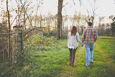 A couple hold hands while walking  along an old farm road.