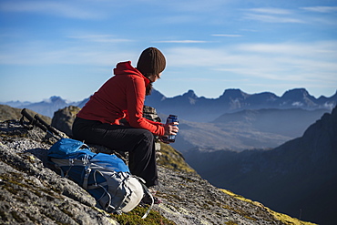 Female hiker takes a break and enjoys mountain views, Moskenesøy, Lofoten Islands, Norway