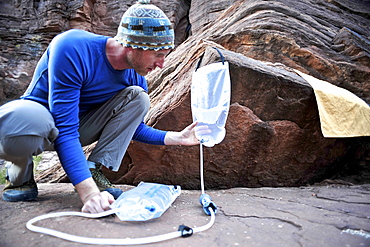 Male hiker filters water on a cliff-pinched patio near Deer Creek Falls in the Grand Canyon outside of Fredonia, Arizona November 2011.  The 21.4-mile loop starts at the Bill Hall trailhead on the North Rim and descends 2000-feet in 2.5-miles through Coconino Sandstone to the level Esplanada then descends further into the lower canyon through a break in the 400-foot-tall Redwall to access Surprise Valley.  Hikers connect Thunder River and Tapeats Creek to a route along the Colorado River and climb out Deer Creek.