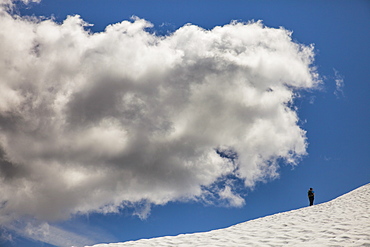 A climber crosses a snowfield in the mountains of British Columbia below a large cloud.