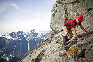 A climber carefully crosses a steep rock slab near the summit of Trio Peak, British Columbia, Canada.