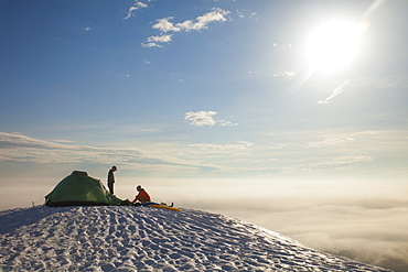 Two climbers sort their gear out beside their tent while camping in the mountains of British Columbia, Canada.