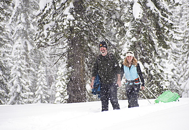 Smiling man and woman snowshoeing in snow storm, Sierra Nevada