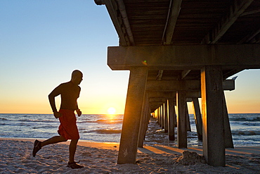 Man running under a pier on the beach at sunset