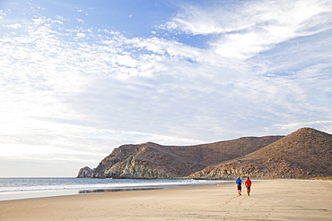 Two people walk down an empty beach under a blue sky, Mexico