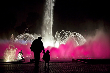 A man and his daughter are silhouetted by a lit-up fountain at Reserva Park in Lima, Peru.