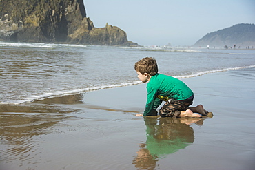 Toddler boy digs in the sand and anticipates the waves on Cannon Beach, Oregon.