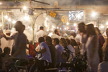 Crowds of people sitting and standing at the food stalls in Jemaa EL Fna square in Marrakesh, Morocco.