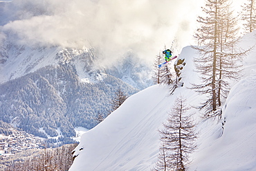 A man jumps down from a rock in the wood, during a cloudy ski morning in San Martino di Castrozza in the Dolomites