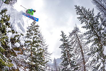 A man jumps down from a rock in the wood, during a cloudy ski morning in San Martino di Castrozza in the Dolomites