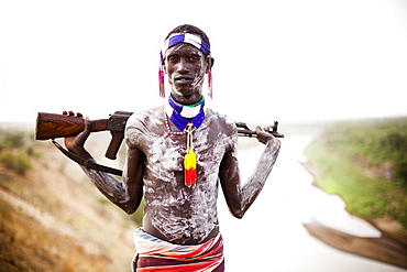 KARO VILLAGE, OMO VALLEY, ETHIOPIA. A young man holds his kalashnikov rifle while overlooking the Omo river in the remote Omo Valley of Ethiopia. (released: MHP_095_MR_RedKere), Ethiopia