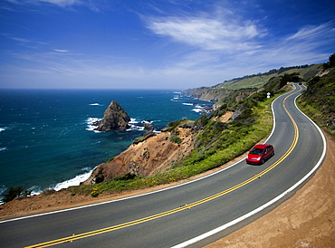 MENDOCINO, CALIFORNIA, USA. A red Prius, a hybrid vehicle, drives on a winding road along the shore of the California coast, United States of America