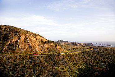 MENDOCINO, CALIFORNIA, USA. A red Prius, a hybrid vehicle, drives on a winding road along the shore of the California coast, United States of America