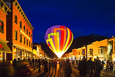 Hot air balloon at dusk with a crowd and building surrounding.