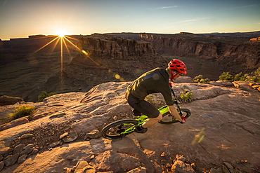 Man mountain biking on a trail in a desert environment at sunset.