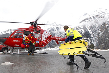 An ambulance paramedic is walking to a rescue helicopter to help an injured mountaineer that was flown down from a mountain after an accident.