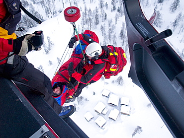 An emergency doctor and patient are being hoisted up to the rescue helicopter after a mountain accident.