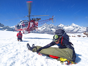 Mountain Rescue Personnel is helping an injured mountaineer in the Swiss Alps. A paramedic is covering the patient to protect it from blown up snow caused by the helicopter.