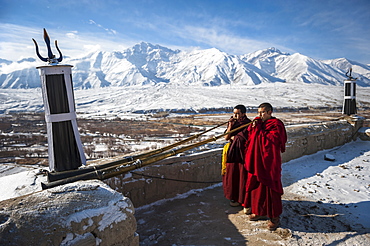 Two monks playing Tibetan trumpets (dungchen) on a roof of Spitok Monastery, Ladakh, India.