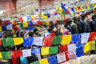 Pilgrims standing in line among prayer flags during Spitok Gustor festival, Spitok, Ladakh, India.