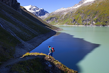 A male hiker on the border of shadow and sunlight, high above the Mooserboden lake, during the Glocknerrunde, a 7 stage trekking from Kaprun to Kals around the Grossglockner, the highest mountain of Austria.