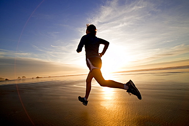 A woman jogs along the wet sand during a beautiful sunset.