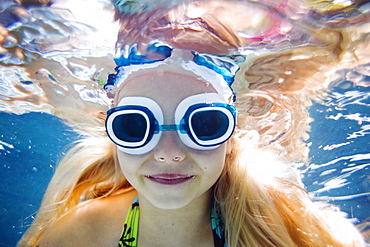 girl swimming in a pool looking at the camera wearing goggles