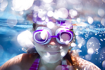 girl swimming in a pool looking at the camera wearing goggles