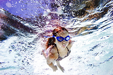 girl swimming towards the camera in a pool, wearing goggles