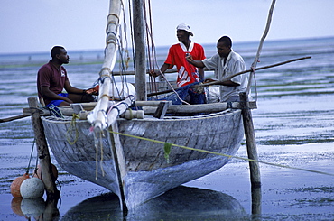 Fishermen sit in a beached dhow on the beach at Paje, on the east coast of Zanzibar Island, Tanzania.