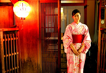 A young Geiko stands in front of the Okiya, (Geisha House), Kyoto, Japan.