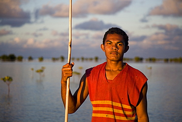 A man holds his spear as he fishes in the mangrove trees at dusk.