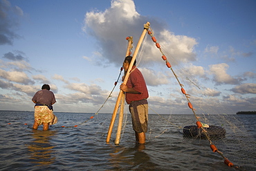 A man holds the ends of a net while a woman collects any trapped fish.