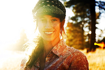 A backlit, young woman smiles and poses for a portrait in a large, grassy field near Flagstaff, Arizona.