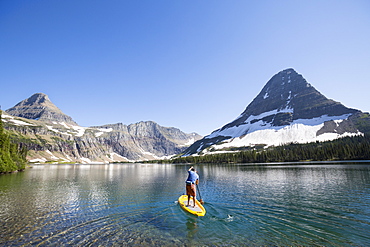 A man stand up paddle boards (SUP) on a calm Hidden Lake in Glacier National Park.