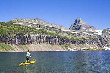 A man stand up paddle boards (SUP) on a calm Hidden Lake in Glacier National Park.