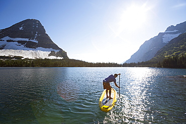 A man stand up paddle boards (SUP) on a calm Hidden Lake in Glacier National Park.