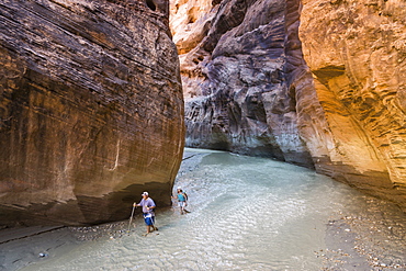 Two people hiking in a canyon with water in it.