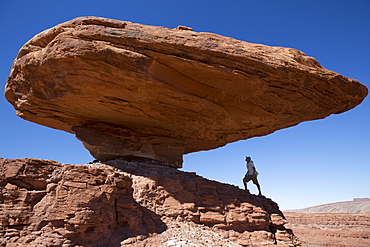 Man standing below a large balanced rock.