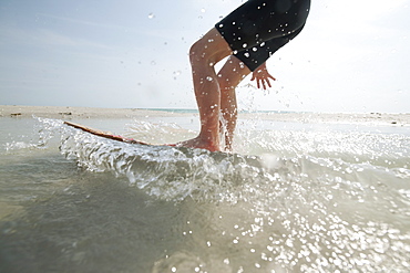 An action shot of a boy on a skim board at the shoreline.