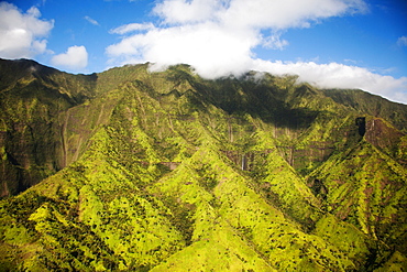 Aerial image of lush green mountain slopes under soft clouds and blue sky.